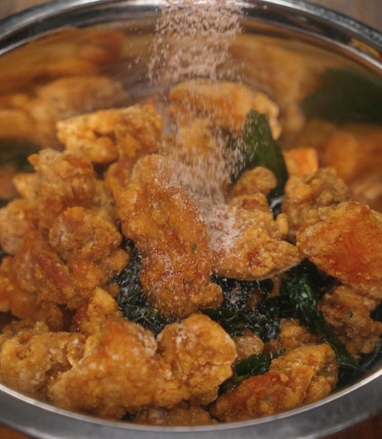 Crispy fried Taiwanese popcorn chicken in a bowl, getting an extra sprinkle of salt, white pepper, and five spice powder.