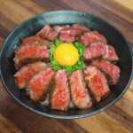 Final hero shot of steak rice bowl featuring seared beef, raw egg yolk, scallions, and glossy glaze served in a rustic bowl.