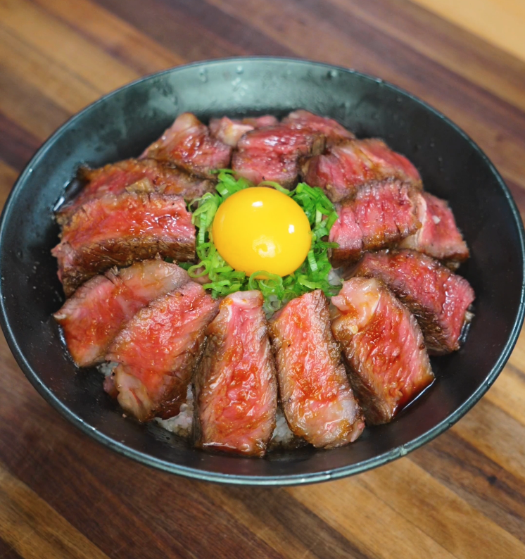 Final hero shot of steak rice bowl featuring seared beef, raw egg yolk, scallions, and glossy glaze served in a rustic bowl.