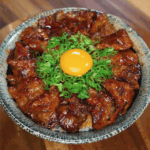 Overhead view of a sticky spicy pork belly donburi topped with finely chopped green onions and a raw egg yolk centered on top, highlighting the vibrant colors and glossy meat glaze.