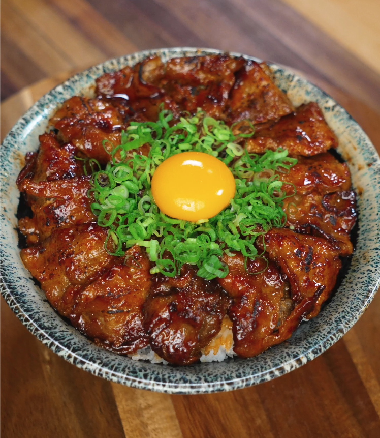 Overhead view of a sticky spicy pork belly donburi topped with finely chopped green onions and a raw egg yolk centered on top, highlighting the vibrant colors and glossy meat glaze.