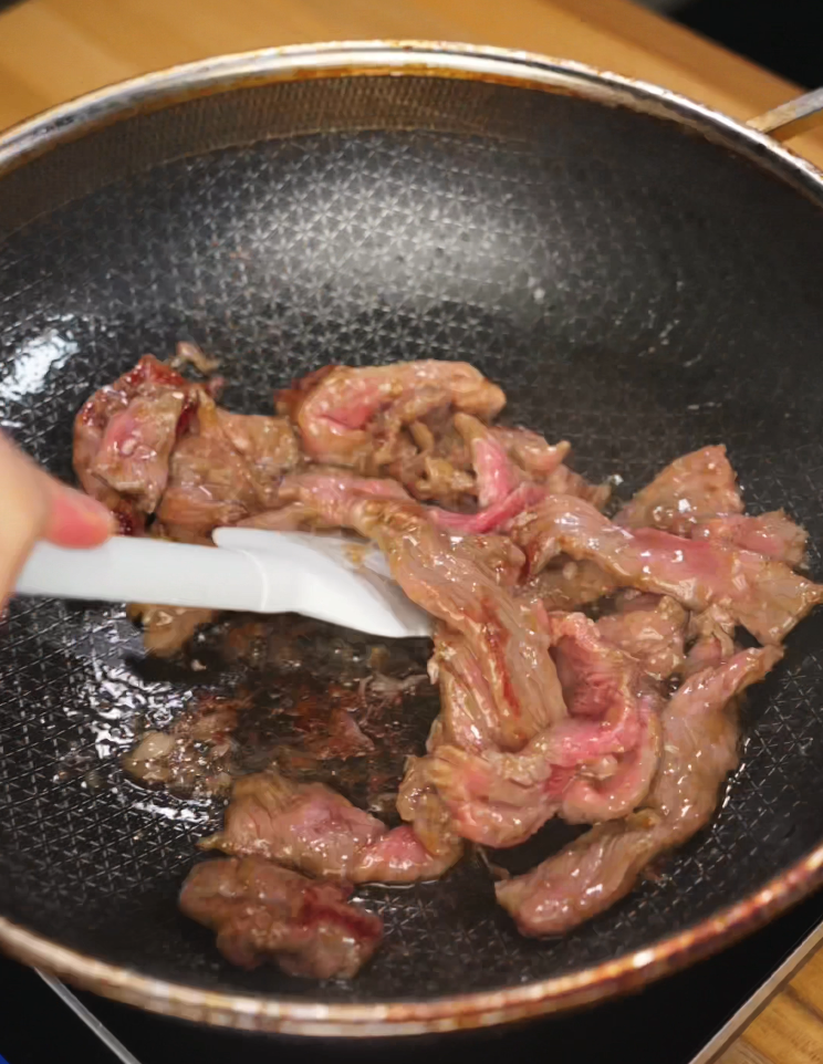 Stir frying marinated beef slices in a hot oiled nonstick pan, with visible sear developing as the beef cooks through.