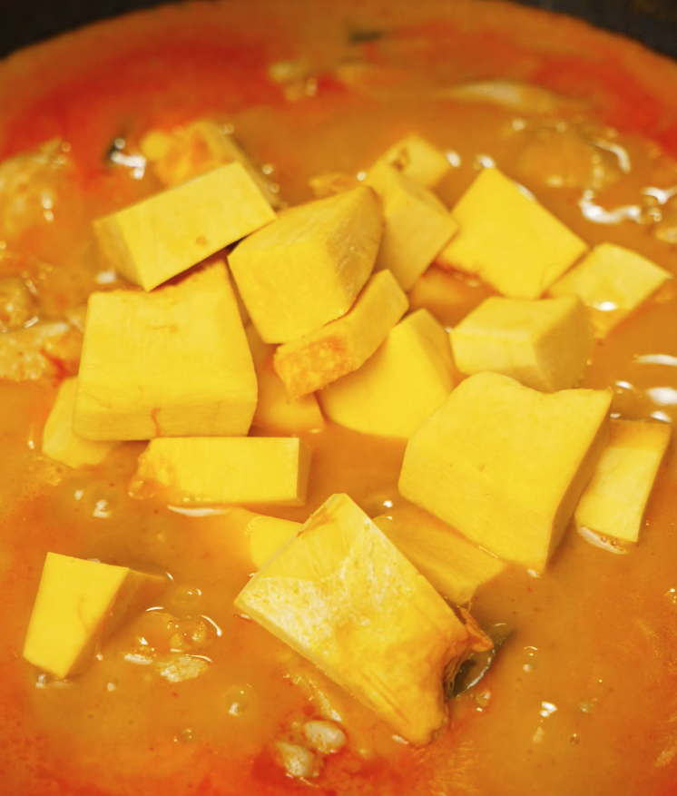 Diced kabocha squash added into the simmering red curry, beginning to soften and absorb the flavorful sauce.
