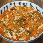 Finished Thai red curry served in a patterned blue and white bowl, garnished with kaffir lime leaves, crushed peanuts, and coconut cream.