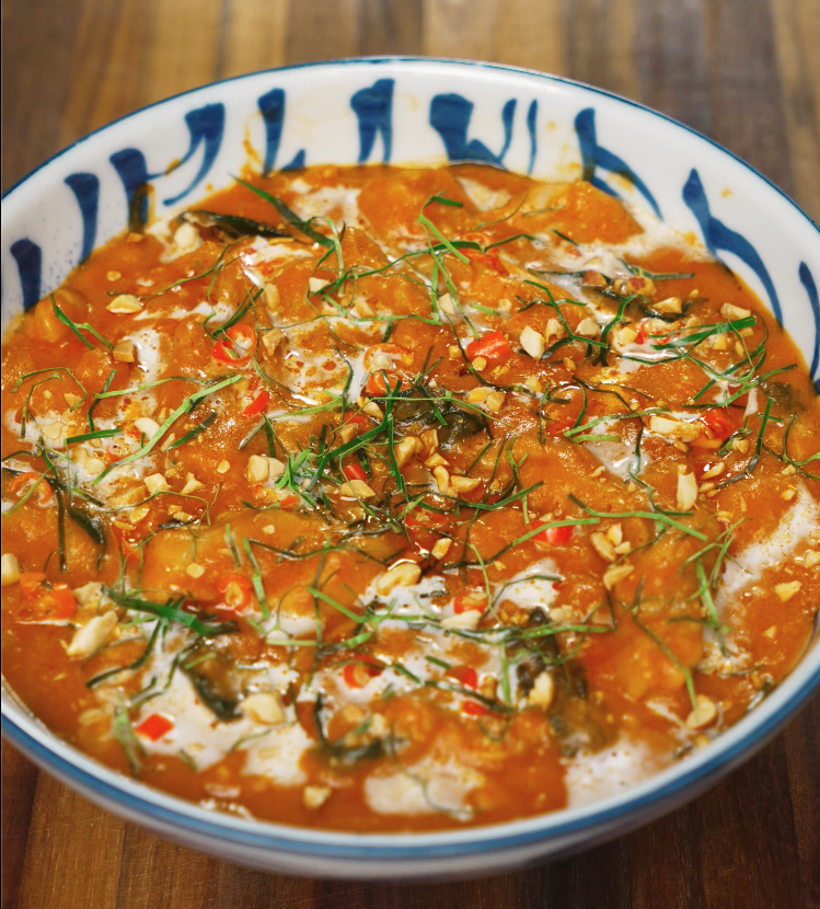 Finished Thai red curry served in a patterned blue and white bowl, garnished with kaffir lime leaves, crushed peanuts, and coconut cream.