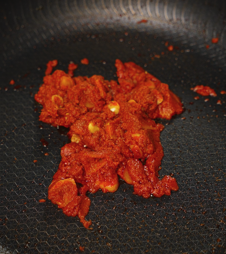 Thai red curry paste with chopped garlic being sautéed in a pan until fragrant and darkened in color.