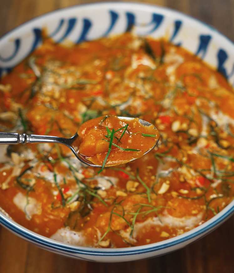 Close-up of a spoonful of Thai red curry showing tender chunks of kabocha, herbs, and creamy sauce above the serving bowl.