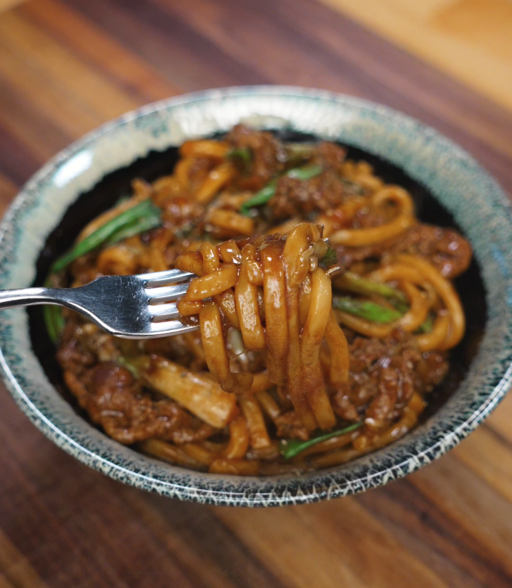 A fork twirling up saucy black pepper beef noodles from a bowl, highlighting the glossy, savory coating and tender beef.