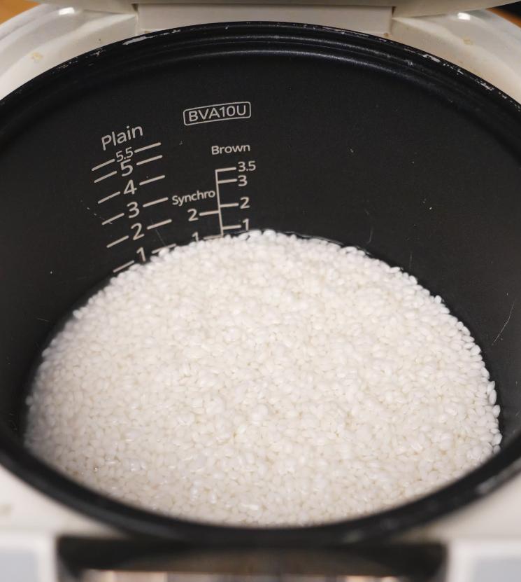 Top-down view of uncooked sticky rice inside a rice cooker, measured and ready to steam.