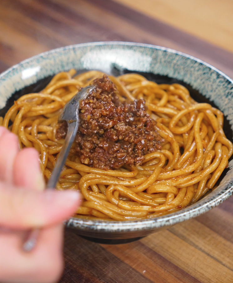 Saucy ground beef is spooned over a bowl of glossy noodles. The dish is ready to be topped with scallions and crispy garlic.