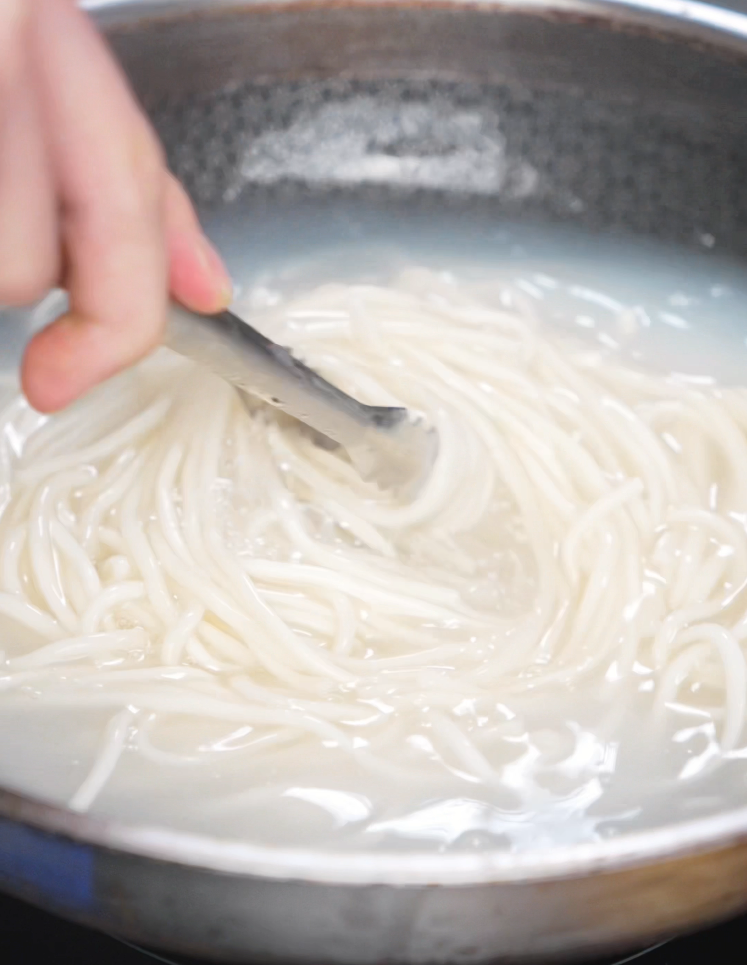A pot of wheat noodles boils on the stove. The noodles are cooked just shy of al dente so they finish perfectly when stir-fried.