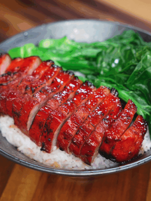 Freshly sliced char siu pork belly rests on top of a bowl of steamed white rice. The glossy glaze glistens under the light, contrasting beautifully with the fluffy grains.