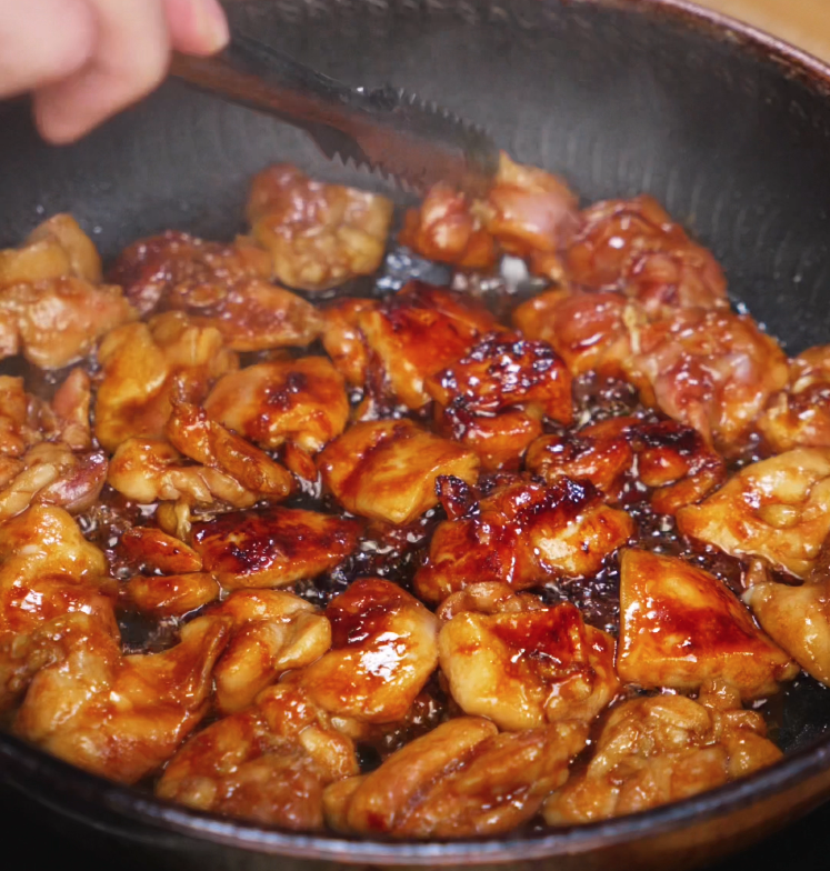Chicken thighs cook in a skillet, bubbling in a thick soy and honey glaze. The pieces are browning evenly with a caramelized coating, indicating rich umami flavor development.