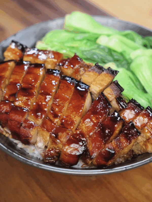 A bowl of white rice topped with glistening, thick-cut slices of honey glazed pork belly. Each piece is lacquered with a caramelized sauce and served alongside vibrant steamed bok choy.