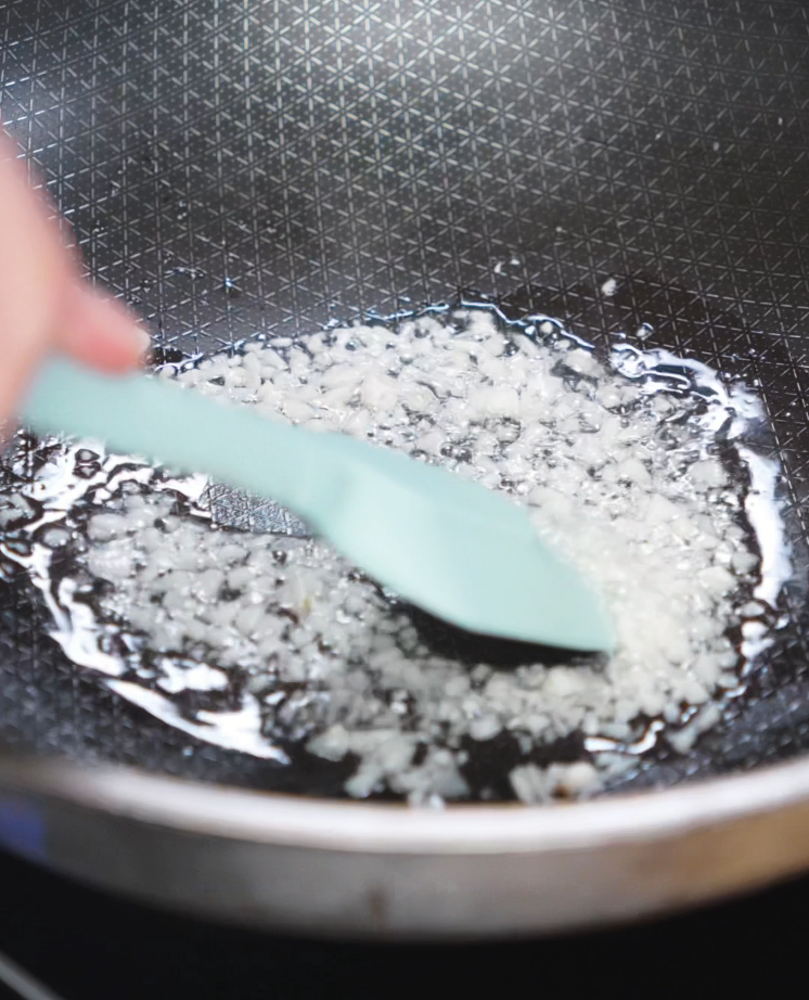 Minced garlic sizzles in oil inside a nonstick skillet. This first stage of garlic sets the base for the savory beef topping.