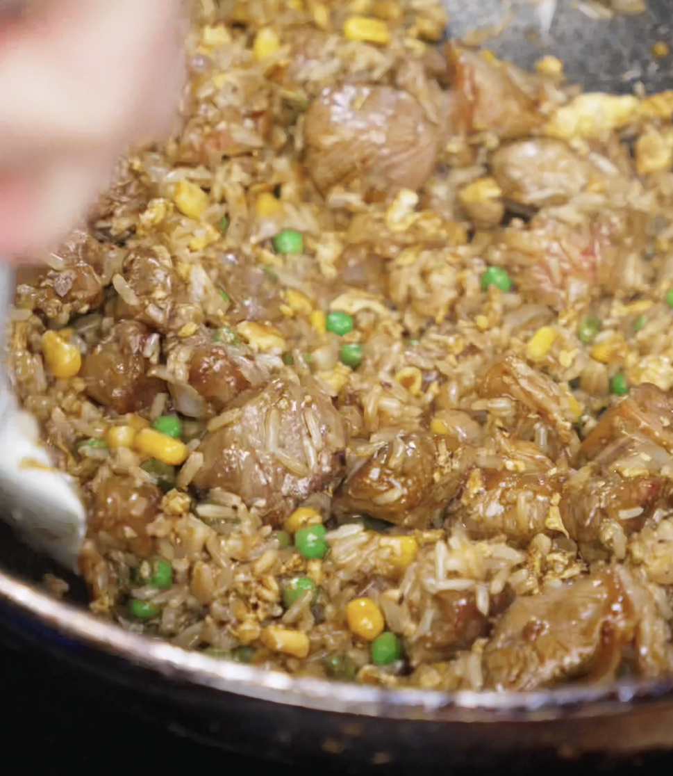 Everything comes together in the wok — beef, rice, scrambled eggs, vegetables, and sauce — being tossed into a cohesive, glossy fried rice dish infused with savory black pepper umami.