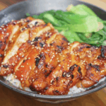 A full view of the completed gochujang glazed chicken bowl, featuring caramelized chicken slices, white rice, and steamed bok choy. The glossy glaze and charred bits promise deep umami and heat.