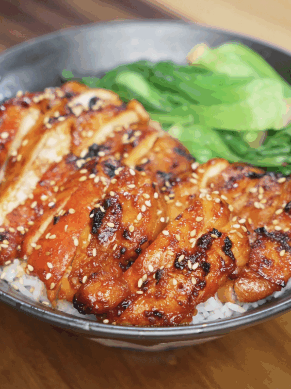 A full view of the completed gochujang glazed chicken bowl, featuring caramelized chicken slices, white rice, and steamed bok choy. The glossy glaze and charred bits promise deep umami and heat.