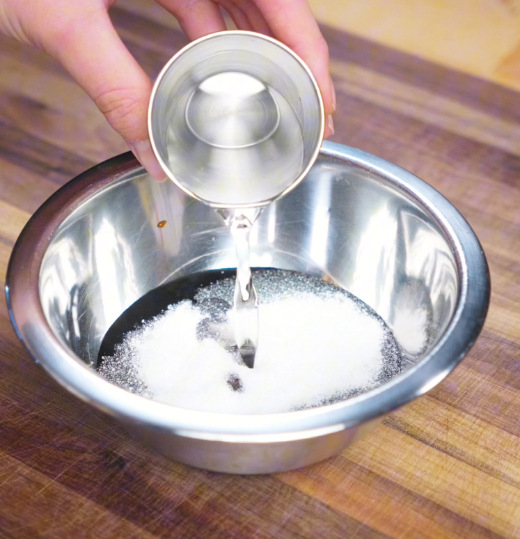A hand pours clear rice vinegar into a metal bowl filled with soy sauce and sugar. This simple sauce brings together sweet, savory, and tangy flavors at the heart of Thai basil chicken.
