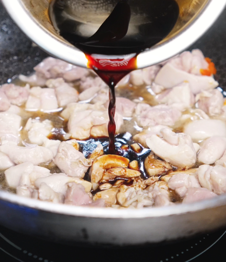 A rich soy-based sauce is poured into the pan of sizzling chicken and garlic chili paste. The sauce immediately bubbles and begins to caramelize.