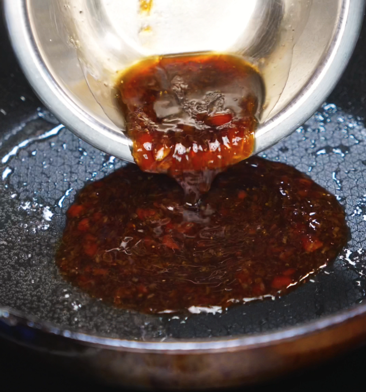 A thick, glossy stream of yakiniku sauce is poured into a hot nonstick pan. Bits of garlic and red chili float in the caramel-colored liquid as it begins to sizzle.
