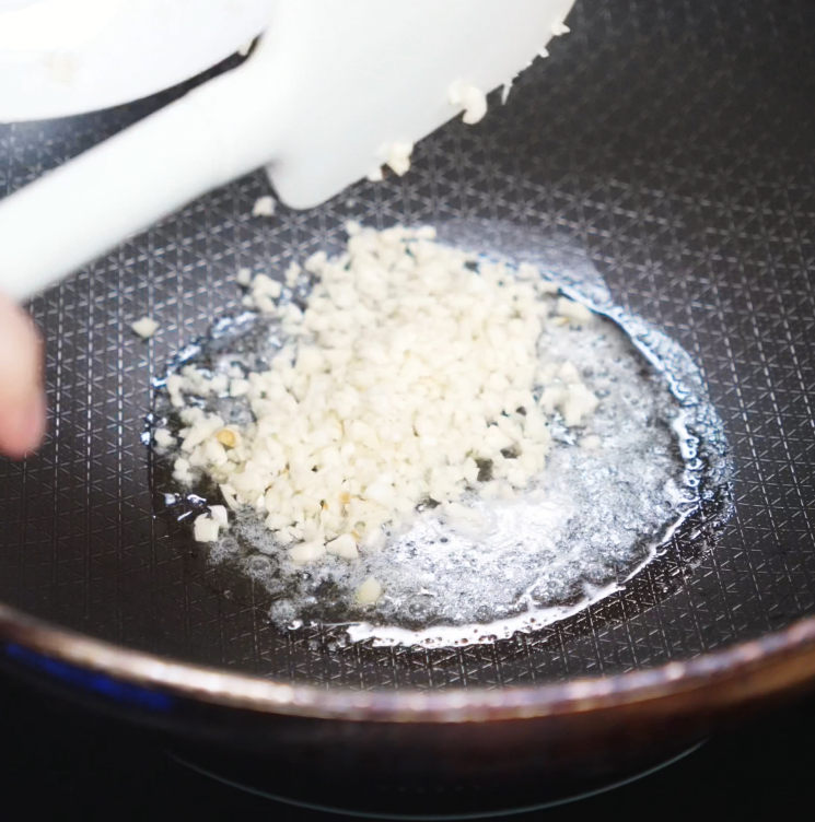Minced garlic is sautéing in melted butter and oil inside a nonstick skillet, releasing a fragrant aroma as it turns lightly golden.