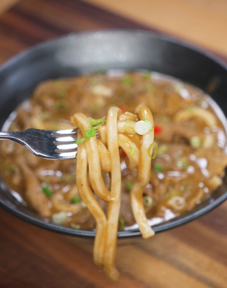 A fork holds a few strands of chewy udon noodles covered in a rich beef curry, which provides the main flavor base of beef curry udon.