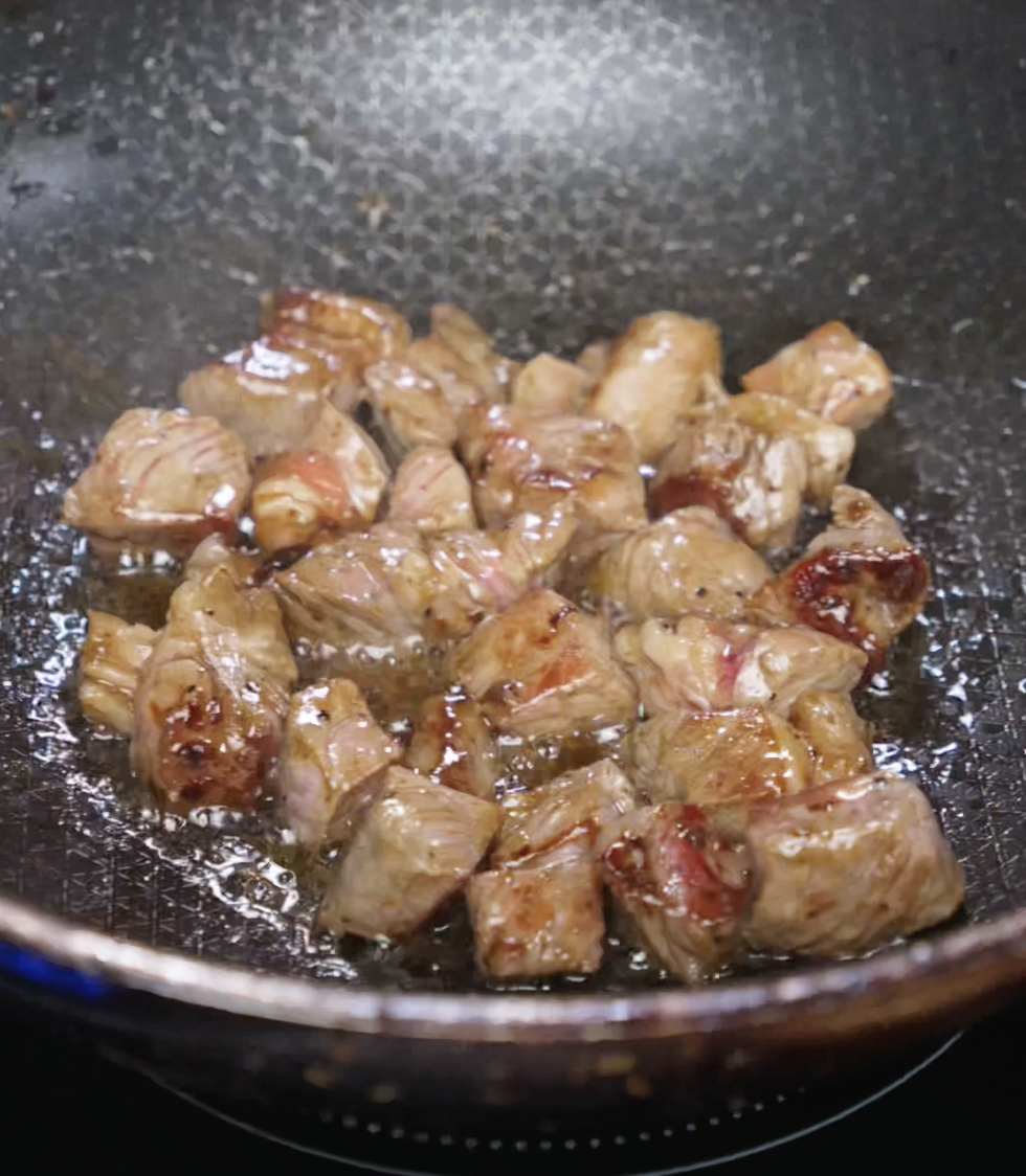 Beef cubes sizzle in a wok as they develop a golden brown crust. The meat is marinated and seared over high heat, locking in moisture and building rich caramelization for the fried rice.