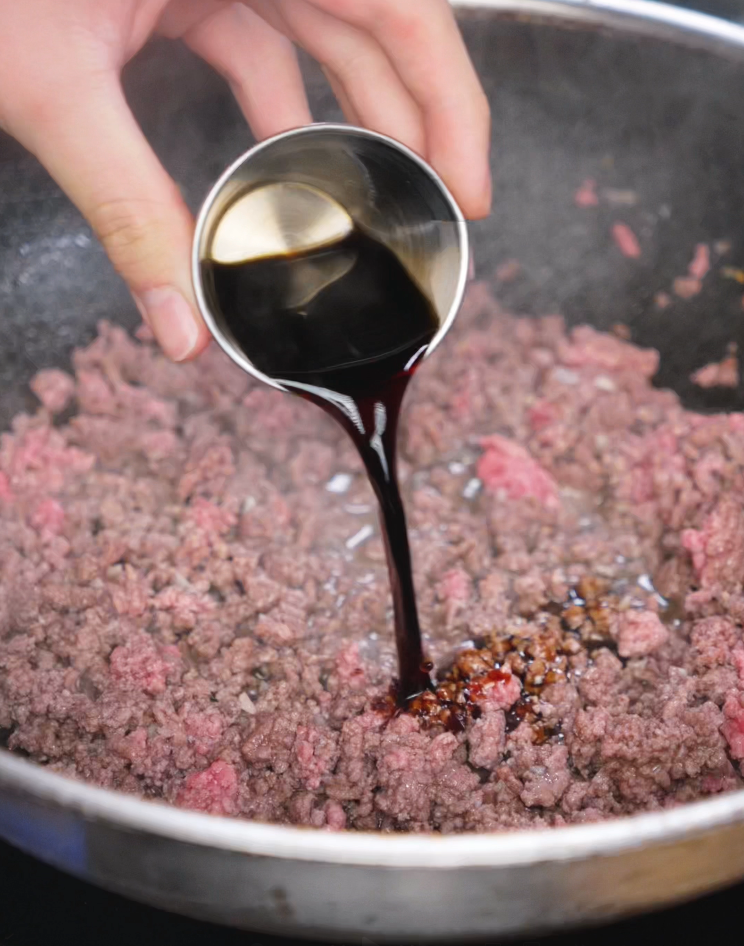 A mixture of soy sauce, oyster sauce, Shaoxing wine, sesame oil, and sugar is added to the beef. The sauce thickens as it coats each crumbled piece.