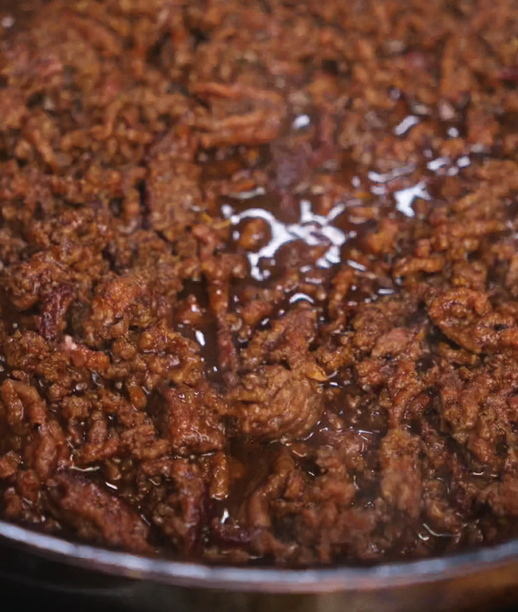 Ground beef simmers in a skillet, coated in thick Japanese BBQ sauce. The meat bubbles gently in the pan, soaking up flavor as it reduces to a glossy, caramelized finish.