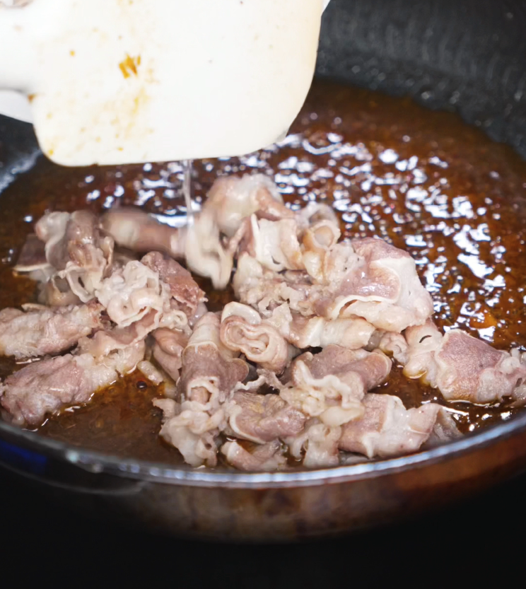 Thin slices of beef are tossed into a pan filled with bubbling yakiniku sauce. The mixture sizzles as it reduces, coating the meat in a glossy layer.