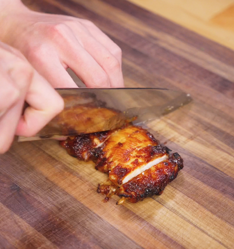 A knife slices through air-fried chicken thighs that are deeply golden and caramelized from the peanut glaze. The juicy interior contrasts with the sticky, seared exterior on a wooden cutting board.