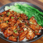 A finished soy butter chicken bowl featuring caramelized chicken pieces glazed in a sticky soy-honey sauce, served over steamed rice with a side of crisp bok choy and garnished with sesame seeds and scallions.
