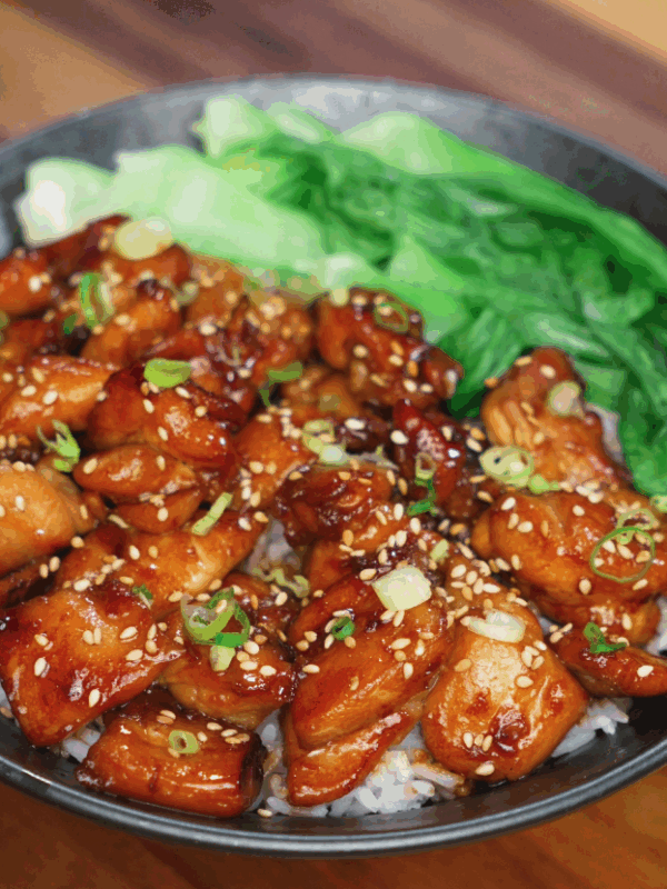 A finished soy butter chicken bowl featuring caramelized chicken pieces glazed in a sticky soy-honey sauce, served over steamed rice with a side of crisp bok choy and garnished with sesame seeds and scallions.