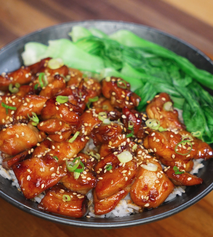 A finished soy butter chicken bowl featuring caramelized chicken pieces glazed in a sticky soy-honey sauce, served over steamed rice with a side of crisp bok choy and garnished with sesame seeds and scallions.