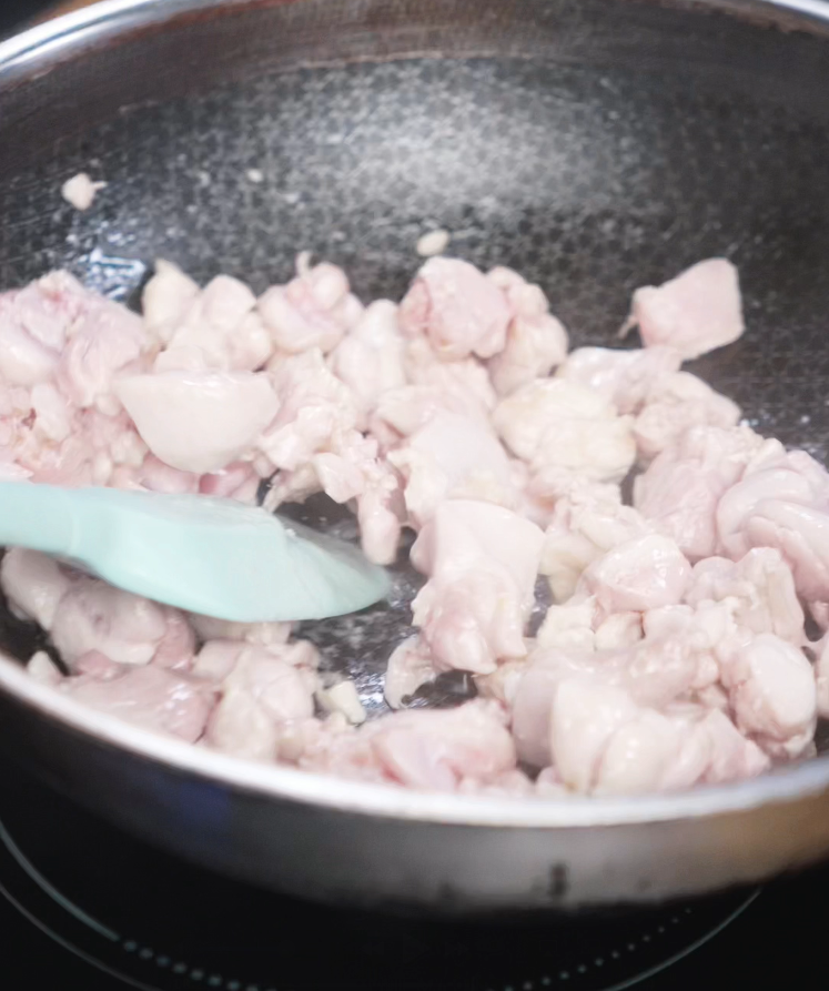 Chopped chicken thigh pieces begin to sizzle in a hot oiled pan. The chicken turns from pink to white as it sears and locks in flavor.