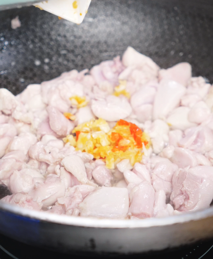 Bright yellow and red chili garlic paste is added to stir-fried chicken in a pan. The fragrance intensifies instantly, coating the chicken in bold flavor.