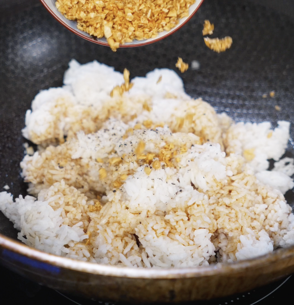 Crispy garlic is poured over day-old white rice in a hot pan, along with soy sauce, salt, and pepper for maximum flavor.
