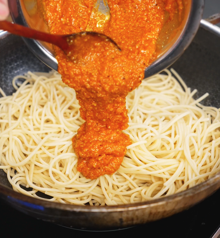 The vibrant orange gochujang egg mixture is poured over cooked spaghetti in a pan, coating each strand in rich, spicy flavor.
