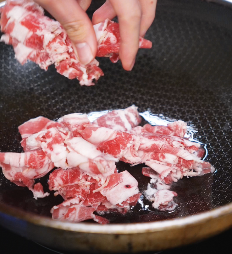 Thinly sliced beef is added to a hot pan with oil to begin the stir-fry, searing quickly for tender, flavorful bites in the fried rice.