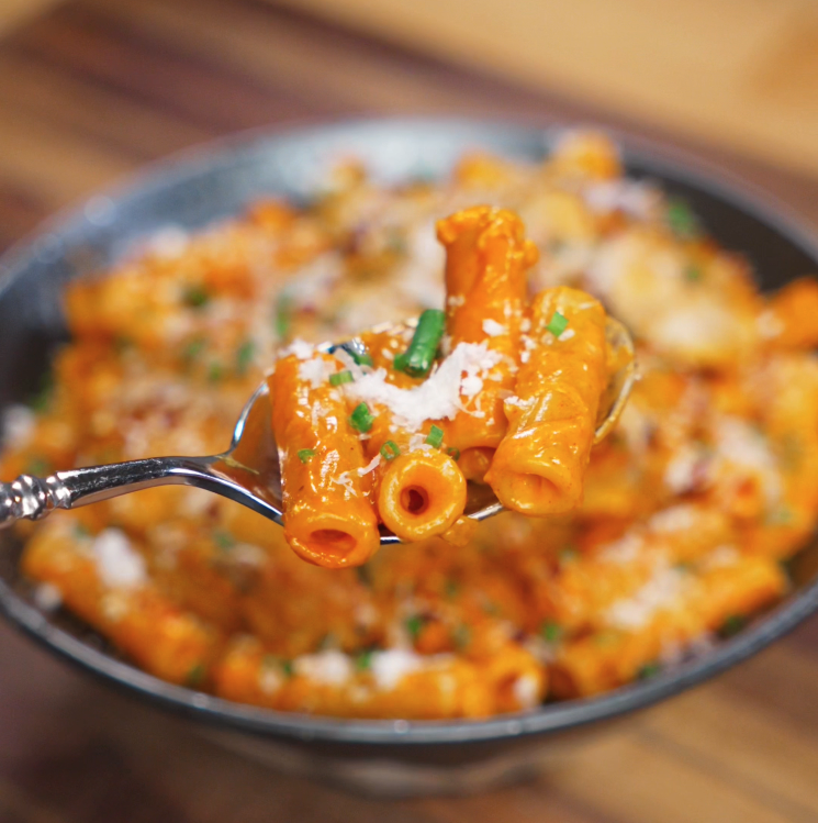 A close-up of a spoonful of rigatoni pasta coated in creamy gochujang sauce, sprinkled with parmesan and flecks of green chives.
