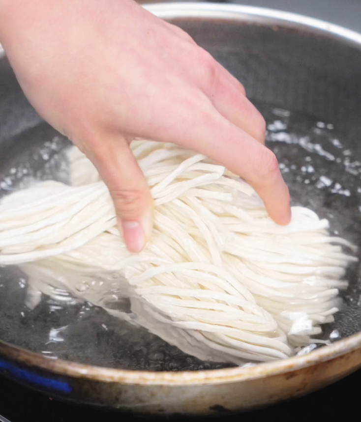A hand lowers a bundle of fresh noodles into boiling water, beginning the quick cook for these savory garlic noodles.