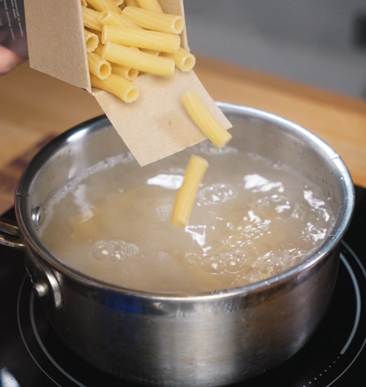 Rigatoni pasta is poured from a box into a pot of vigorously boiling salted water, just moments before being cooked to al dente perfection.