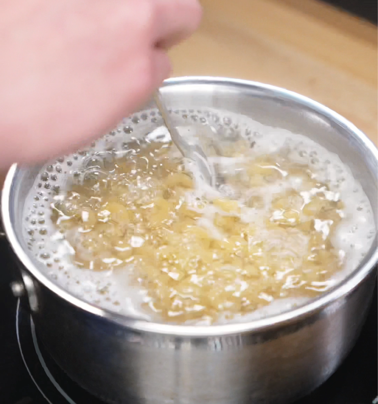 Elbow macaroni boils in a pot of salted water, stirred occasionally to prevent sticking before being added to the sauce.