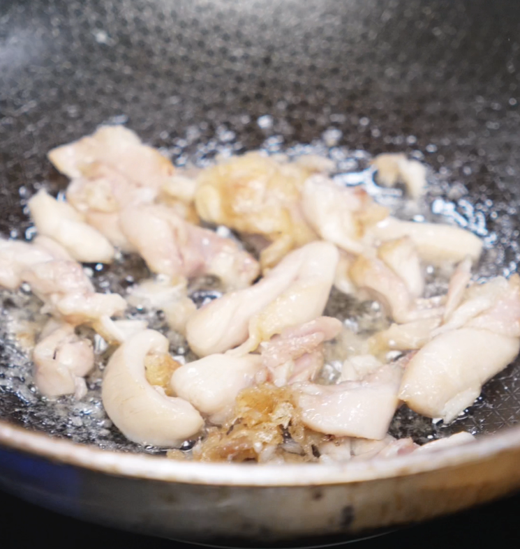 Thin slices of marinated chicken thighs sizzle in a hot pan, forming the rich and juicy base of the black pepper chicken.