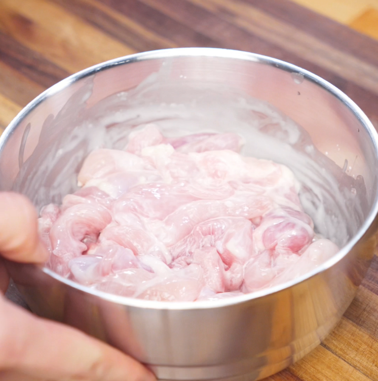 Thinly sliced raw chicken thighs marinate in a bowl with cornstarch, shaoxing wine, and salt, ready to be stir-fried for yaki udon.