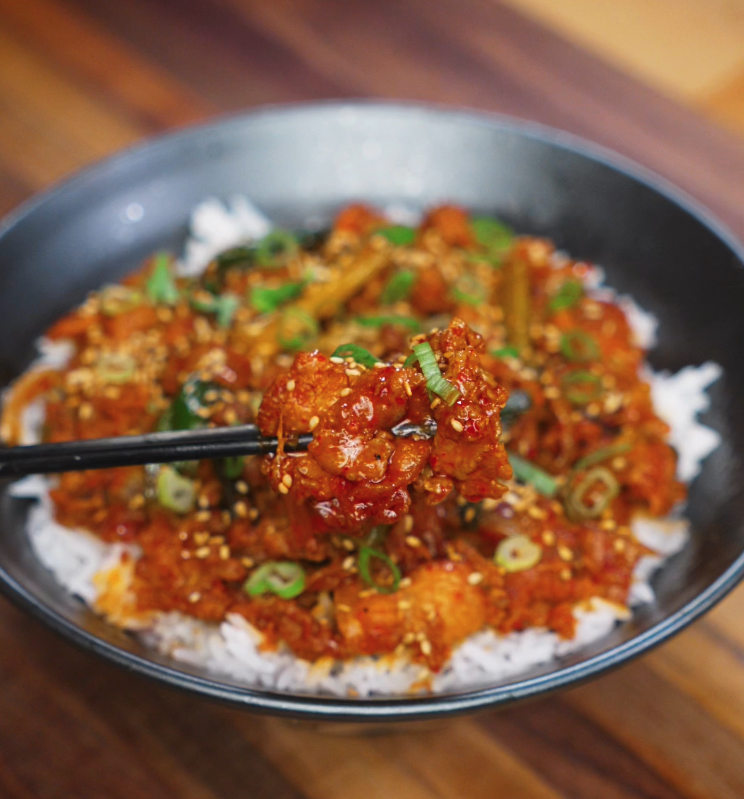 A saucy bite of pork bulgogi is lifted from the bowl with chopsticks, glistening with gochujang glaze and flecked with scallions and sesame.