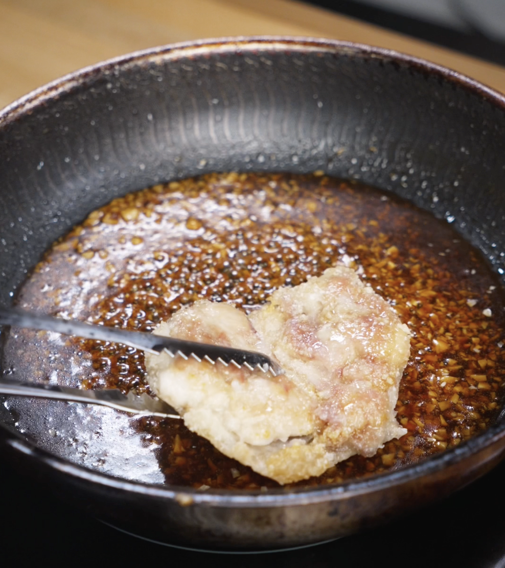 Fried chicken thighs are returned to the pan and tossed in the thickened honey garlic sauce until fully coated and glossy.
