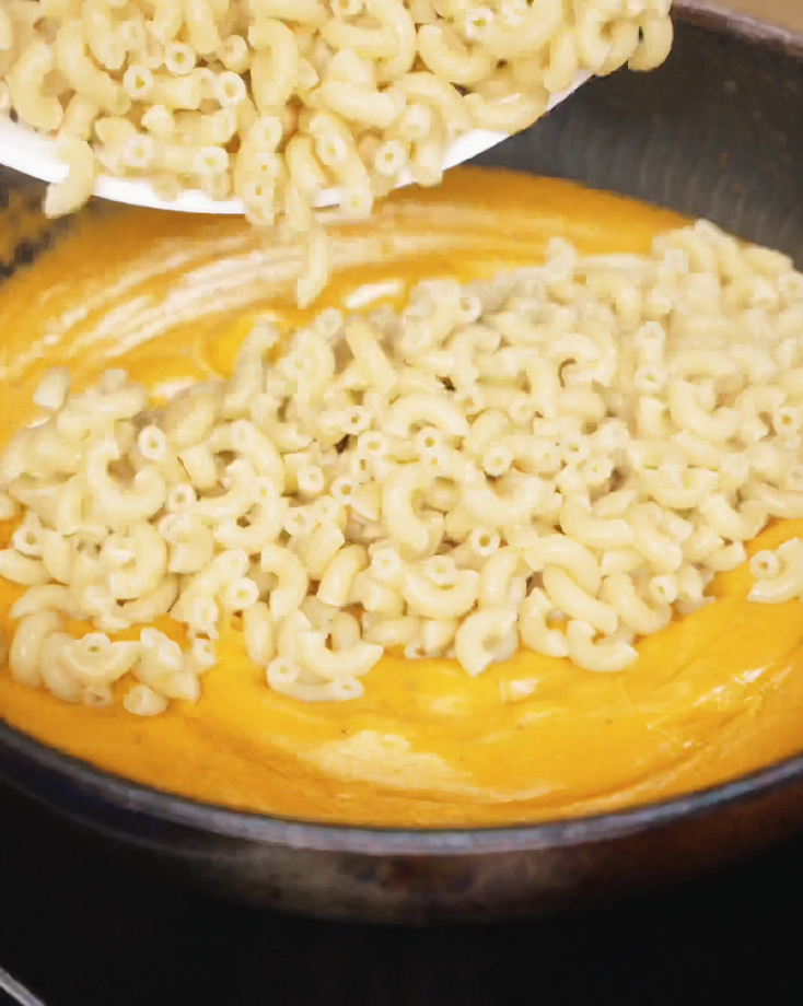Cooked macaroni is poured into the gochujang cheese sauce, ready to be coated in the rich, spicy, and cheesy mixture.