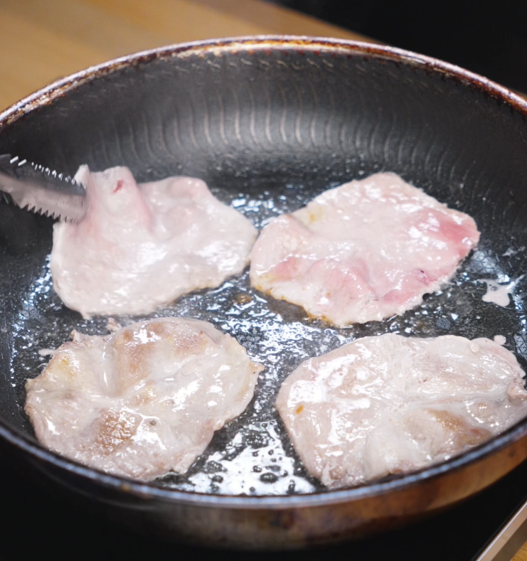 Slices of raw pork sizzle in a hot skillet, beginning to brown as they cook for the ginger pork bowl.